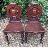 A PAIR OF VICTORIAN MAHOGANY HALL CHAIRS With carved backs over serpentine fronted seats with canted