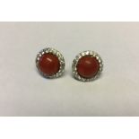 A PAIR OF 18CT WHITE GOLD, RED CORAL AND DIAMOND STUD EARRINGS The round coral cabochons claw set to
