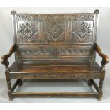 AN 18TH CENTURY OAK SETTLE The panelled back carved with lozenge and stylized foliate decoration,