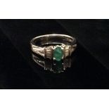 A 14CT WHITE GOLD, DIAMOND AND COLOMBIAN EMERALD RING The single oval cut emerald flanked by two