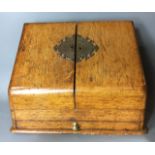 A LATE 19TH CENTURY OAK STATIONARY BOX Having sloping front doors fitted with an elaborate brass