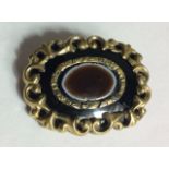 A VICTORIAN PINCHBECK AGATE AND ENAMEL OVAL MOURNING BROOCH With a scrolled edge, set with an
