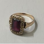 A YELLOW METAL, AMETHYST AND SEED PEARL RING The single emerald cut amethyst contained within a