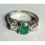 A 14CT WHITE GOLD AND EMERALD RING The single oval cut emerald flanked by two round cut diamonds,