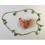 A PINK CORAL BROACH OF FLORAL FORM Along with a yellow metal necklace hung with green jade beads.
