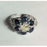 A 14CT WHITE GOLD, DIAMOND AND SAPPHIRE CLUSTER RING The single round cut diamond surrounded a row