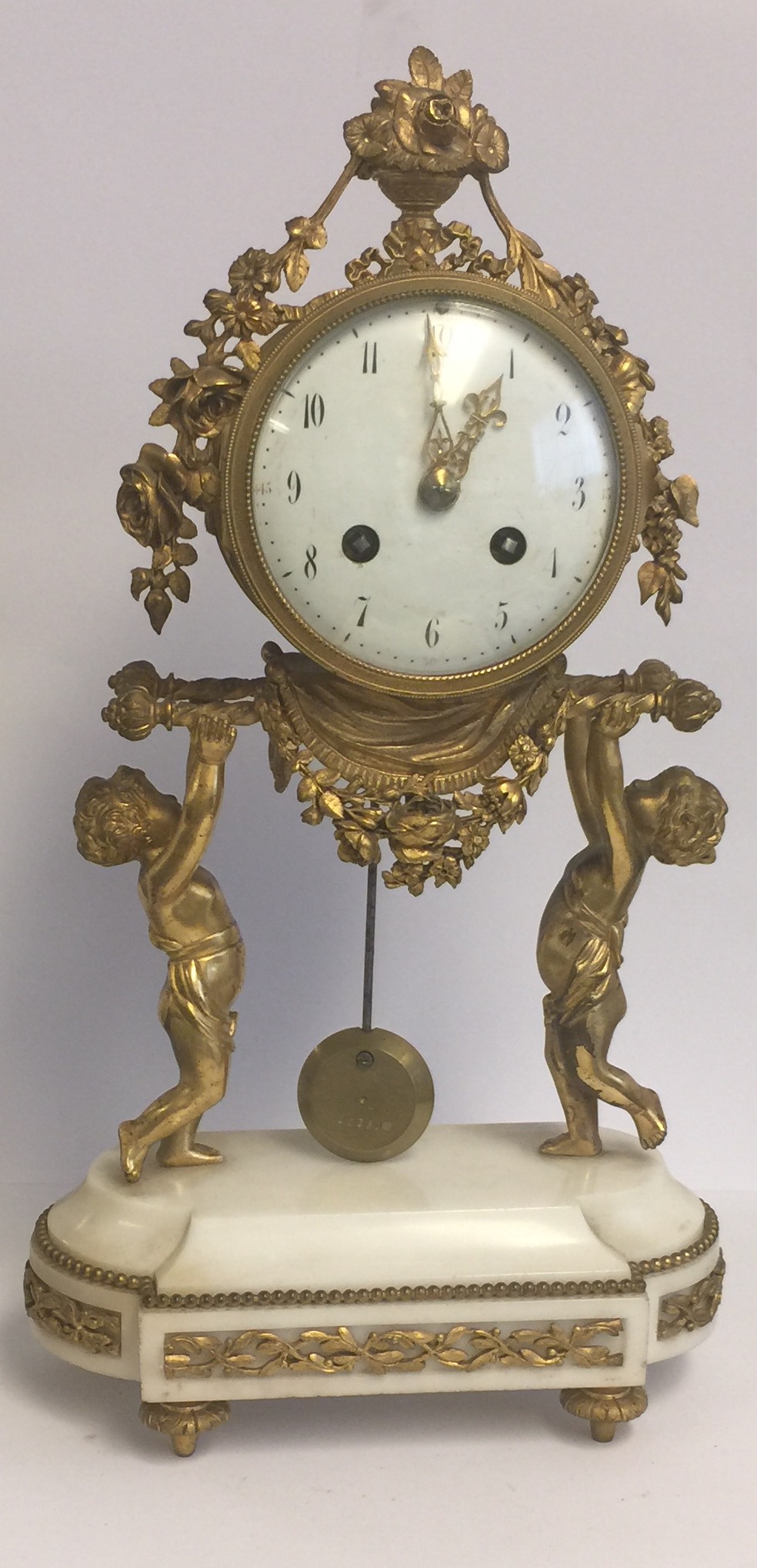 A 19TH CENTURY GILT BRONZE AND WHITE MARBLE DRUM CLOCK Held aloft by two putti. (38cm x 21cm x 9cm)