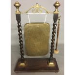 AN EARLY 20TH CENTURY BRASS DINNER GONG On an oak stand with barley twist supports. (48cm x 88cm)