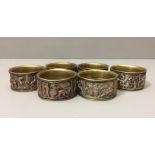 A SET OF SIX EARLY 20TH CENTURY BRASS NAPKIN RINGS Decorated with white metal panels, depicting