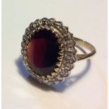 A VINTAGE 9CT GOLD, GARNET AND DIAMOND RING Having a single oval cut garnet surrounded by a row of