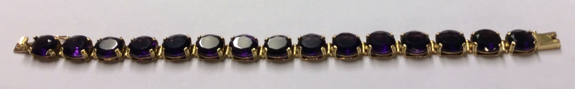 AN 18CT GOLD AND AMETHYST BRACELET Having a single row of oval cut amethysts set in articulated