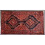 A red ground Middle Eastern rug, with central double medallion and latch hook design within multiple