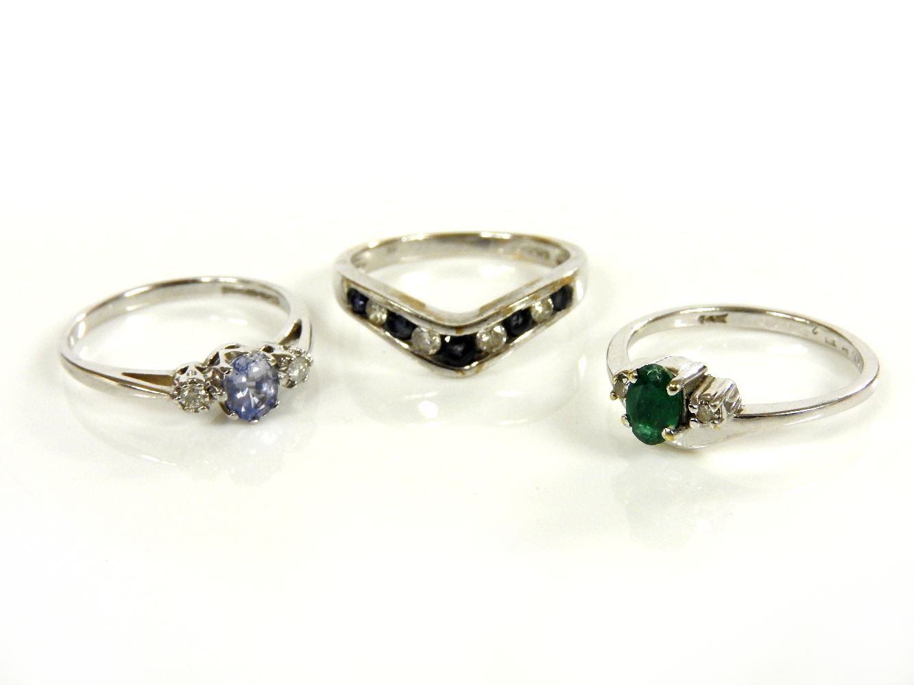 A 9ct white gold three stone sapphire and diamond ring, a white three stone emerald and diamond