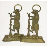 Two brass door stops, each in the form of a dancing bear, beside a ragged staff, inscribed '