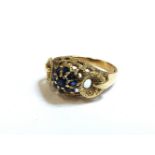 A 9ct gold sapphire cluster ring, with textured circular buckle shoulders