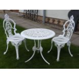 A white painted cast aluminium garden table and two chairs, the table 70cm diameter