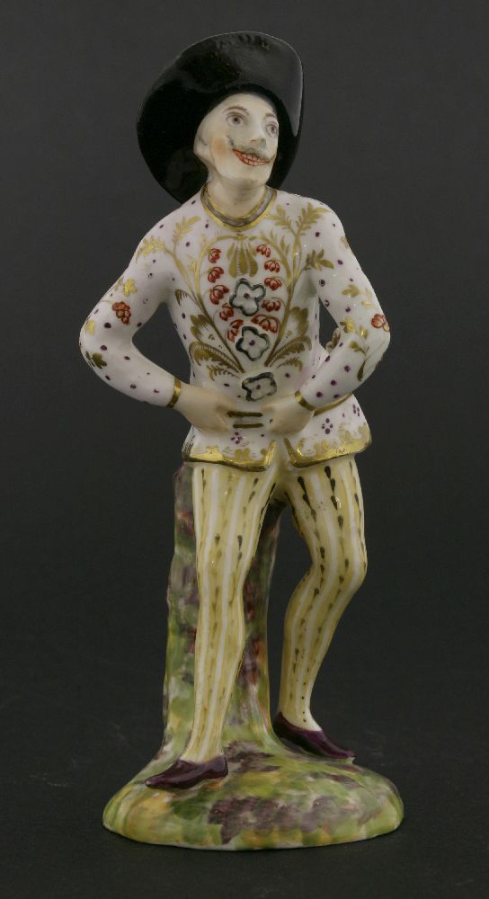 An English ceramic harlequin figure,with slapstick tucked into his belt, raised on a naturalistic