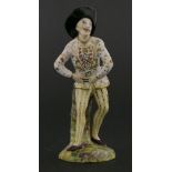 An English ceramic harlequin figure,with slapstick tucked into his belt, raised on a naturalistic