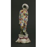 An Italian Cozzi ceramic harlequin figure,leaning up against a tree stump, mounted on shaped