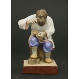 A Russian ceramic seated figure,19th century, of a cobbler mending a shoe, on rectangular mark, with