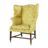 An antique wing back armchair,with embroidered rich yellow fabric upholstery, raised on mahogany
