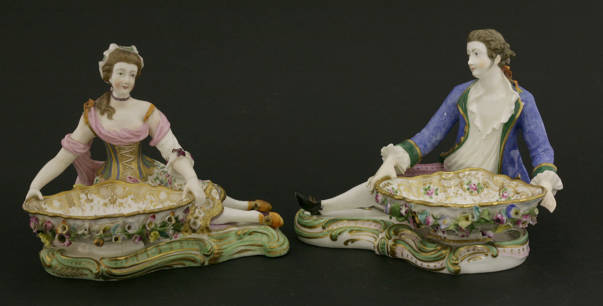 A pair of Minton reclining figures,both cradling a flower-encrusted bowl, on shaped rocaille