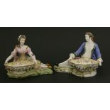 A pair of Minton reclining figures,both cradling a flower-encrusted bowl, on shaped rocaille