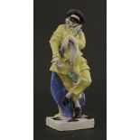 A ceramic figure, of harlequin wearing a yellow coat and trousers, standing on chequered base,