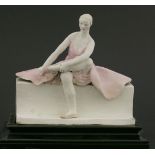 A Chelsea Cheyne figure,a ballerina seated on a bench, with one leg crossed over her other leg,