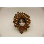 A Continental porcelain miniature of a young boy with a pierced and carved Black Forest frame