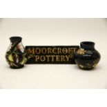 Three items of Moorcroft pottery, to include two small vases and a name plaque, all decorated with
