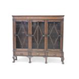 An oak bookcase with three sliding glazed doors, on a cabriole leg stands, 156cm wide, 32cm deep,