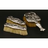 A matched three-piece set of silver-backed dressing table brushes, one hard brush embossed with