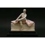 A Chelsea Cheyne figure,a ballerina seated on a bench, with one leg crossed over her other leg,