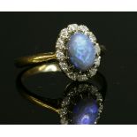 A black opal and diamond oval cluster ring, c.1950,with an oval cabochon black opal, claw set to the