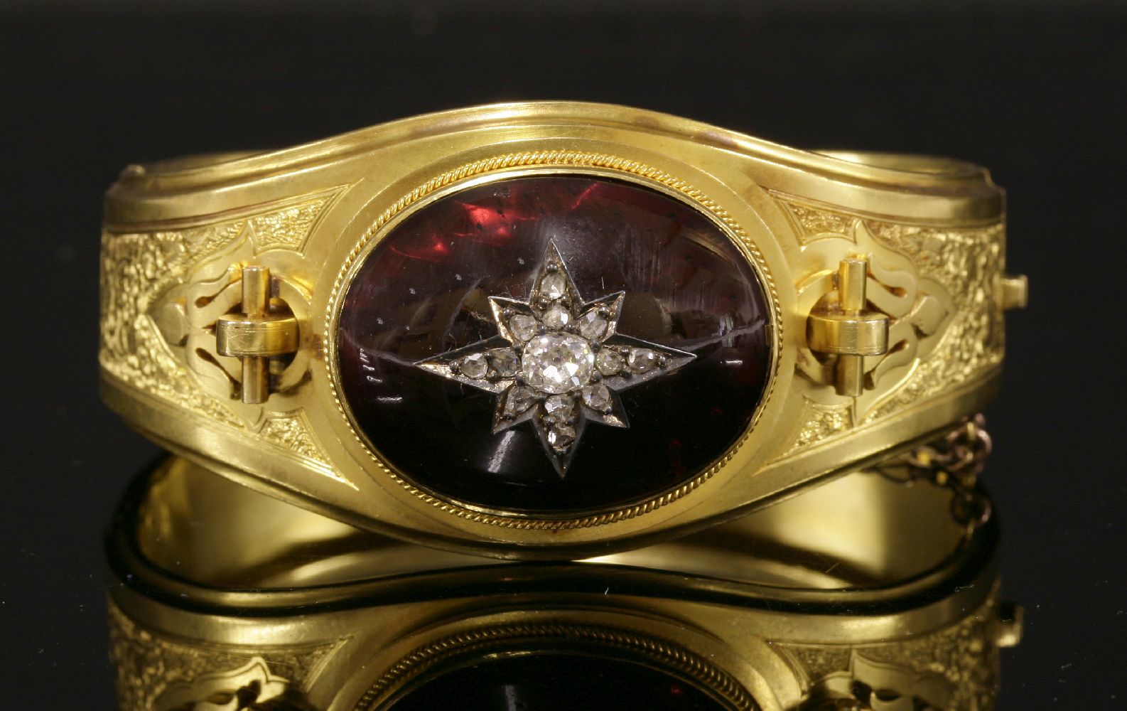 A Victorian gold garnet and diamond hinged bangle,with a central oval cabochon garnet with applied