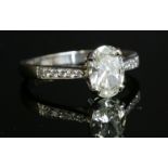 A platinum single stone diamond ring,with diamond set shoulders, with an oval diamond four claw