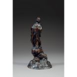 ƒ STATUETTE DE RAKANen bronze de belle patine sombre, représenté debout sur un rocher, vêtu d'un