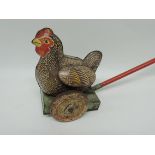 A push-along tinplate toy chicken with moving wings, wood handle and realistic "clucking" sound when