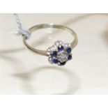 A 9ct white gold dress ring of flower head form, set with a central illusion set diamond with a