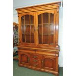 A modern light wood cabinet, having moulded cornice, pair of glazed doors enclosing two shelves, two