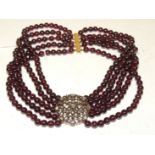 A five strand, garnet bead choker necklace, with a large yellow metal clasp set with a cluster of