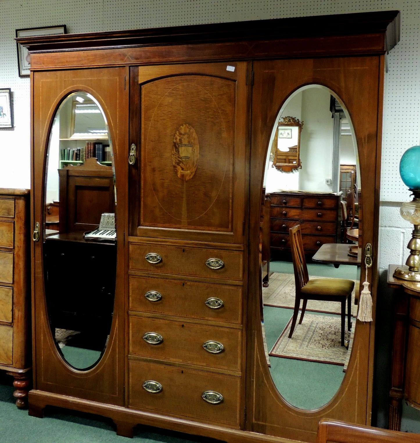 An Edwardian inlaid mahogany compactum, having two oval bevelled mirrored doors, enclosing fabric