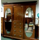 An Edwardian inlaid mahogany compactum, having two oval bevelled mirrored doors, enclosing fabric