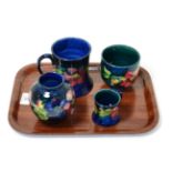 Four pieces of Walter Moorcroft pottery, in the Clematis pattern including two mugs (one a.f.) and