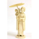 A Japanese Ivory Okimono, Meiji period, as a mother holding a parasol, her son on her shoulder, on a