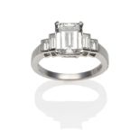 A Platinum Diamond Ring, an emerald-cut diamond in a white claw setting, to shoulders each set