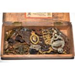 A small wood box containing assorted military cap badges, shoulder titles, rank pips and buttons