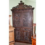 An early 20th century ornately carved oak corner cupboard with shield and bishop's miter crest rail,