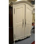 A cream painted armoire of recent date with moulded canopy top above panel doors enclosing hanging